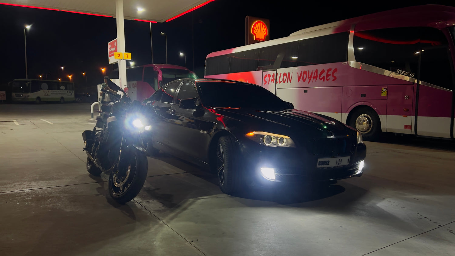 Car and motorcycle with a bus in the background at night.